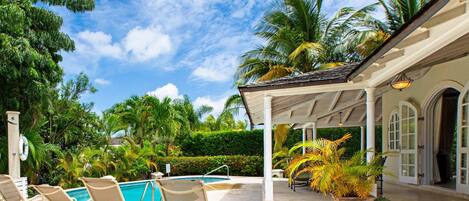 A pool area with lounge chairs, a covered patio, and palm trees.
