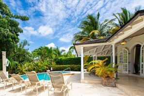 A pool area with lounge chairs, a covered patio, and palm trees.