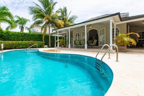 A swimming pool with a covered patio area, palm trees, and a building with arched windows. - Palm Ridge 2A (Westmoreland)