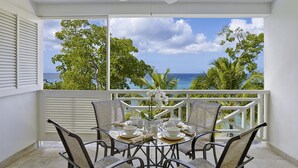A balcony with a table set for dining, overlooking a tropical beach and ocean. - Waterside 303 (Paynes Bay)