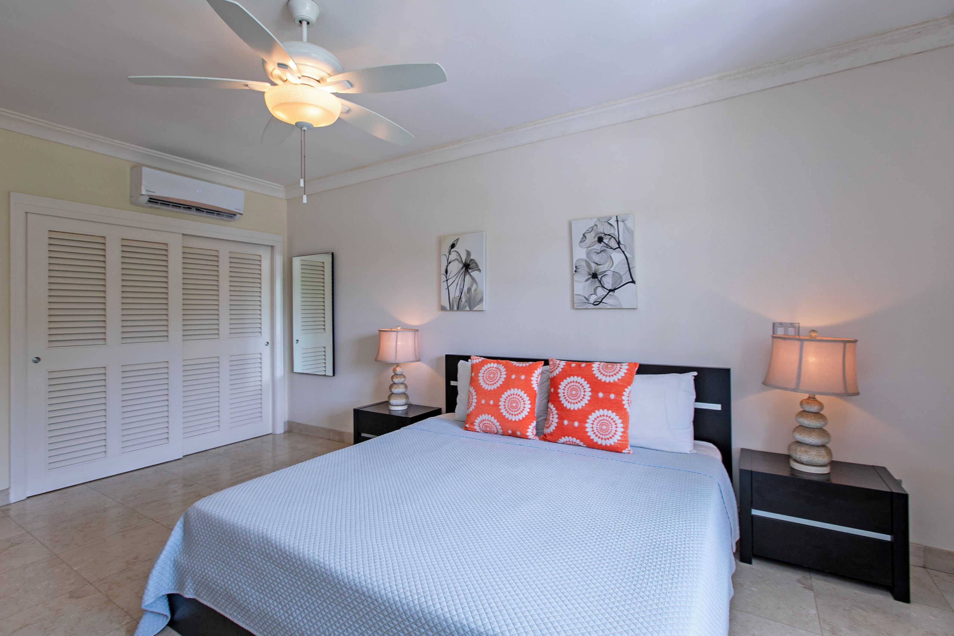 A bedroom with a bed, two nightstands with lamps, a ceiling fan, and artwork on the wall.