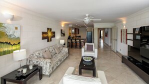 A modern living room with a patterned sofa, a coffee table, and a dining area in the background. - Waterside 303 (Paynes Bay)
