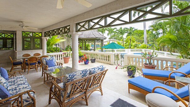 A covered outdoor seating area with wicker furniture, a glass table, and potted plants. - Blue Haven (Bowling Alley Hill)