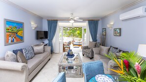 A living room with a sofa, armchairs, a coffee table, and a TV. There is a window with curtains and a view of the outdoors. - Blue Haven (Bowling Alley Hill)