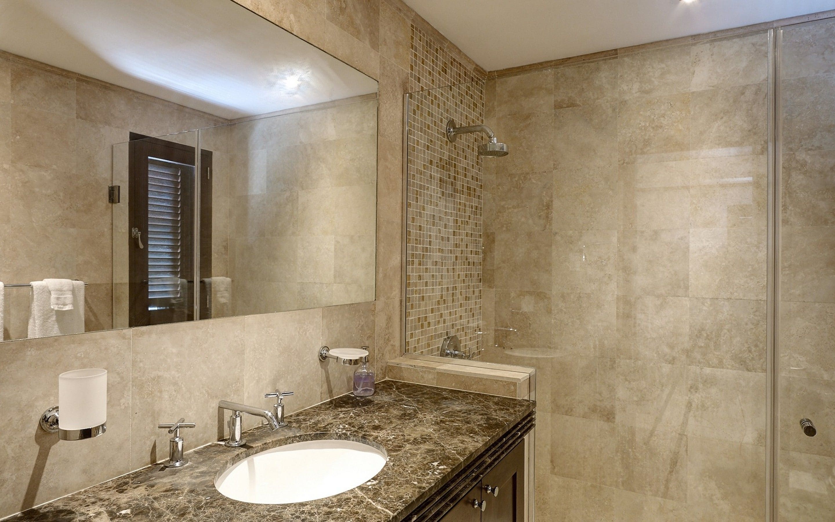 Une salle de bain avec un grand miroir, un lavabo, une douche et un mur recouvert de carreaux.