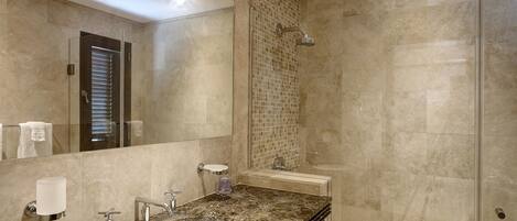 A bathroom with a large mirror, a sink, a shower, and a tiled wall.