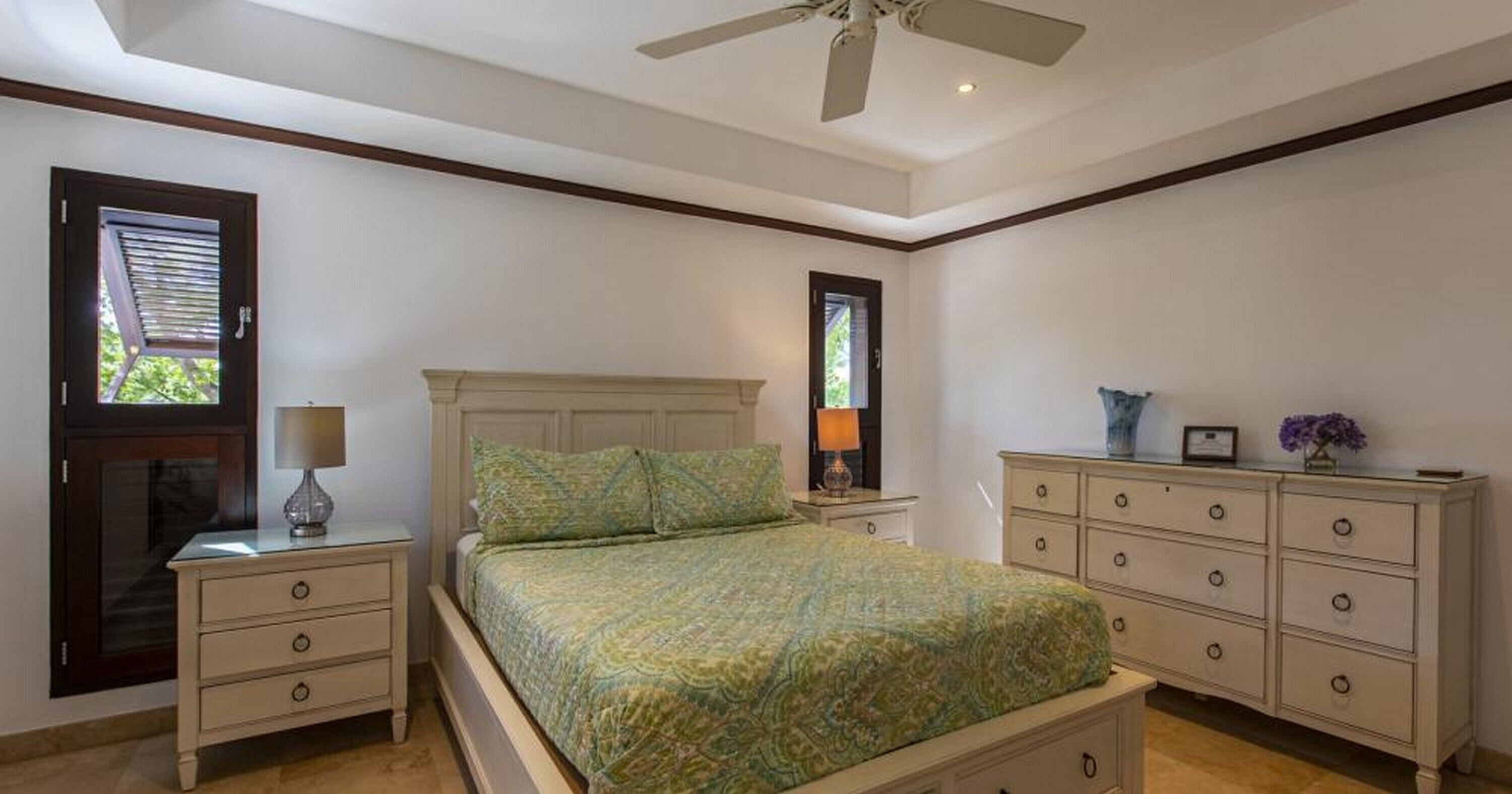Un dormitorio con cama, mesitas de noche, cómoda y ventilador de techo.