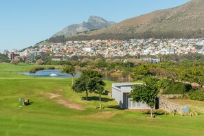 A golf course with a pond, a stone wall, and a building with a flat roof. - V&A Waterfront Luxury Residences - WHosting (Cape Town)