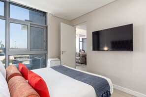 A modern hotel room with a large bed, a flat-screen TV, and a view of the outside through large windows. - V&A Waterfront Luxury Residences - WHosting (Cape Town)