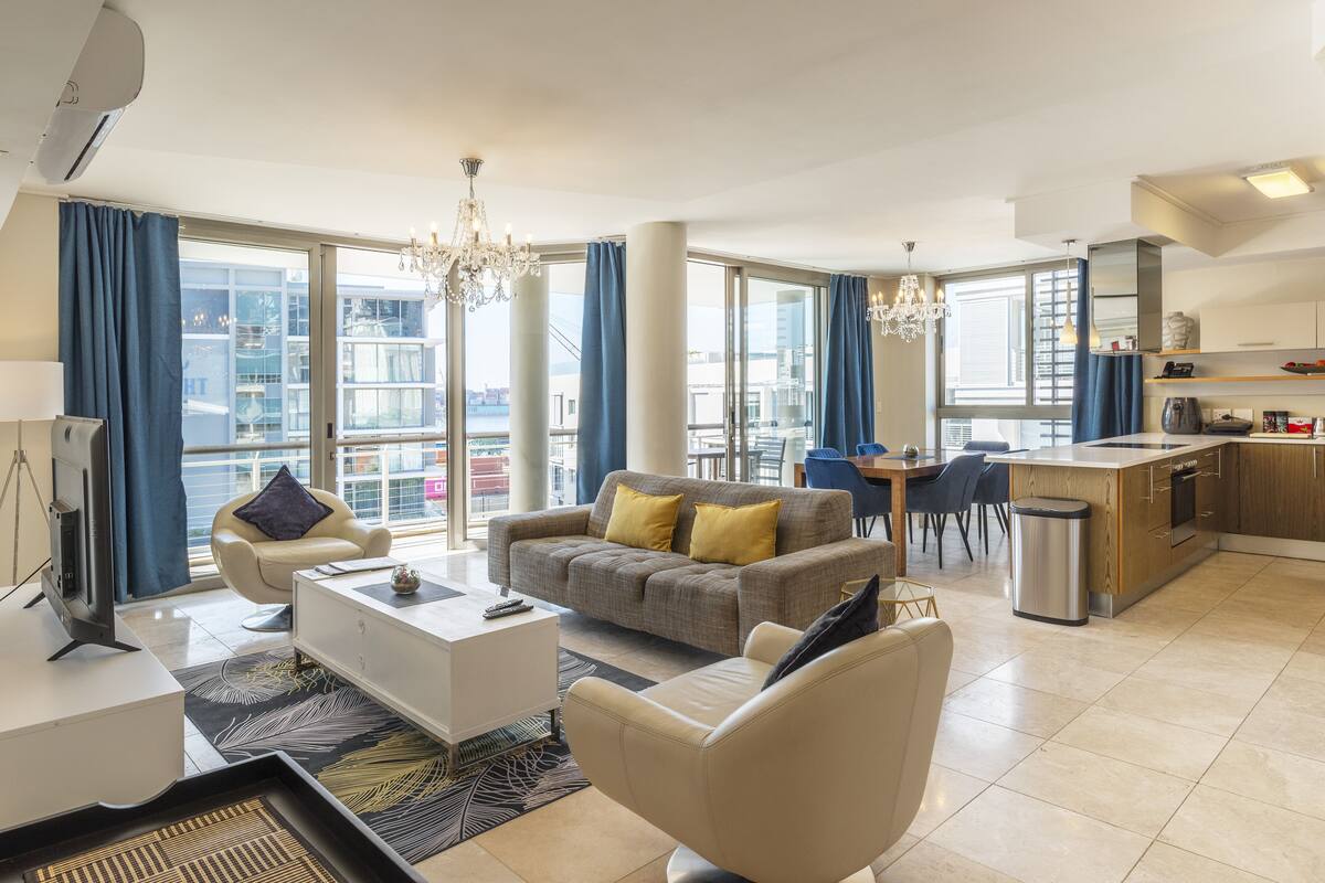 A modern hotel room with a living area, dining space, and kitchenette.