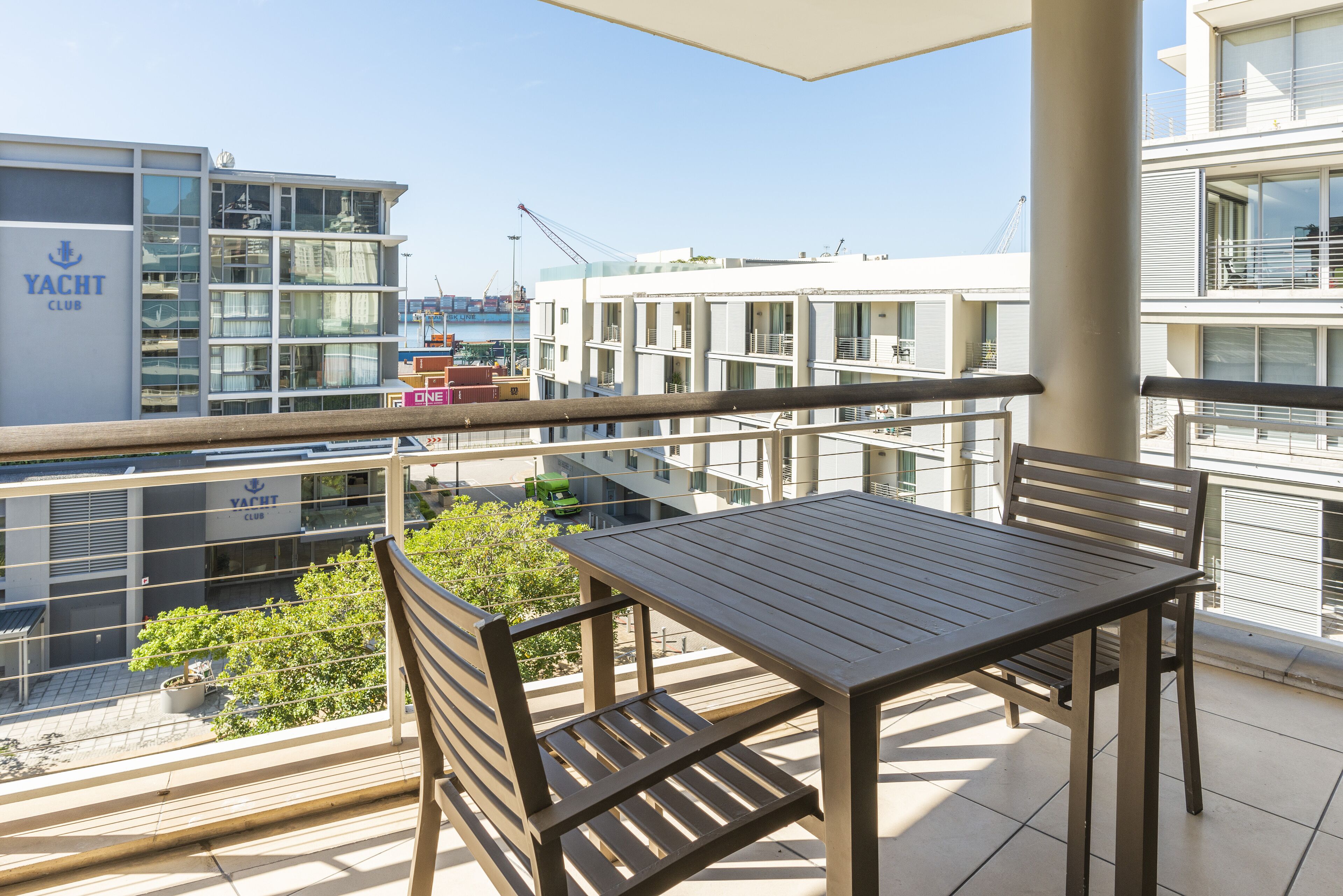 A balcony with a table and chairs, overlooking a marina with yachts and a building labeled 'YACHT CLUB'.