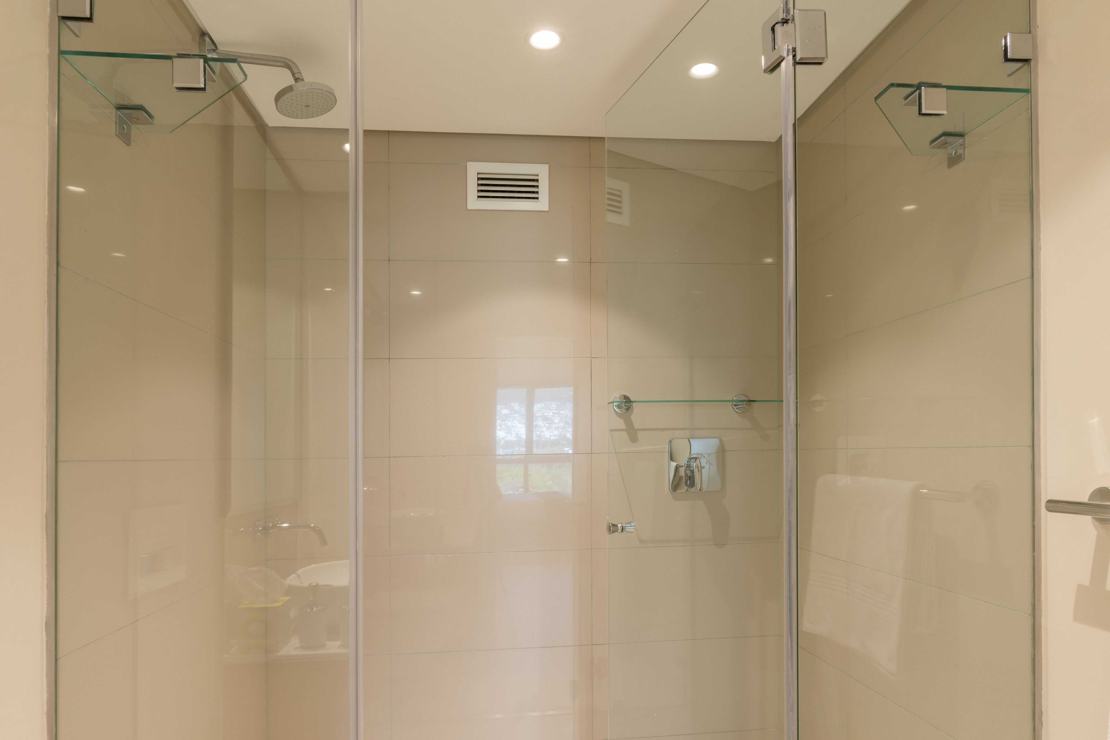 A modern shower with glass doors, a glass shelf, and a towel rack.