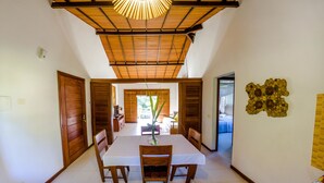 A dining area with a table set for two, wooden doors, a ceiling fan, and a view into another room. - Trancoso Residence (Porto Seguro)