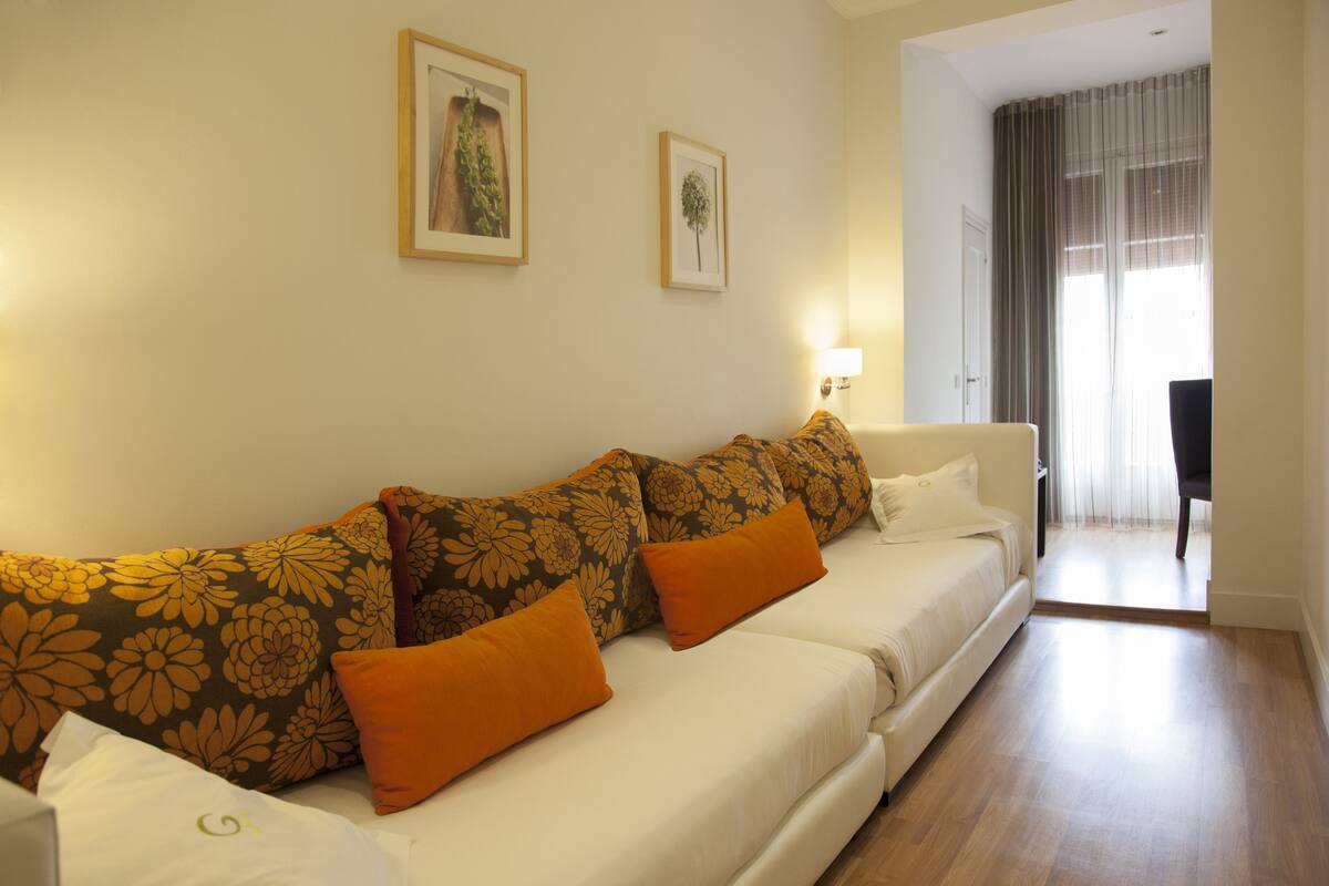 A modern living room with a sofa set, framed artwork on the walls, and a view into another room through a doorway.
