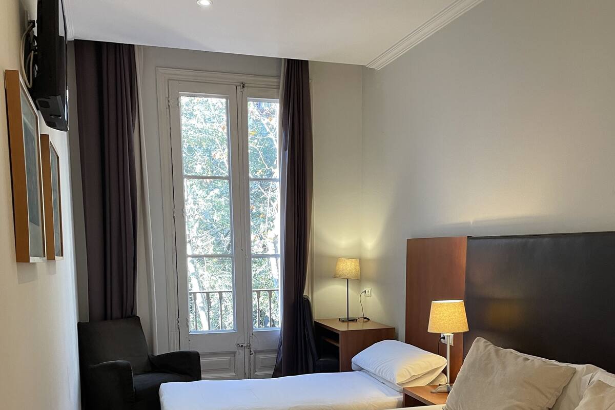 A hotel room with two beds, a desk, a chair, a TV, and a window with curtains.