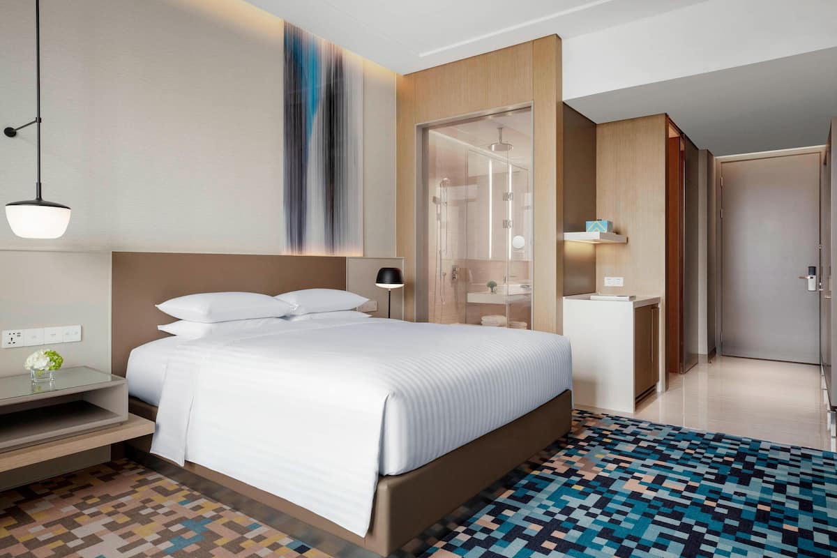 A modern hotel room with a large bed, bedside table, and a shower area.