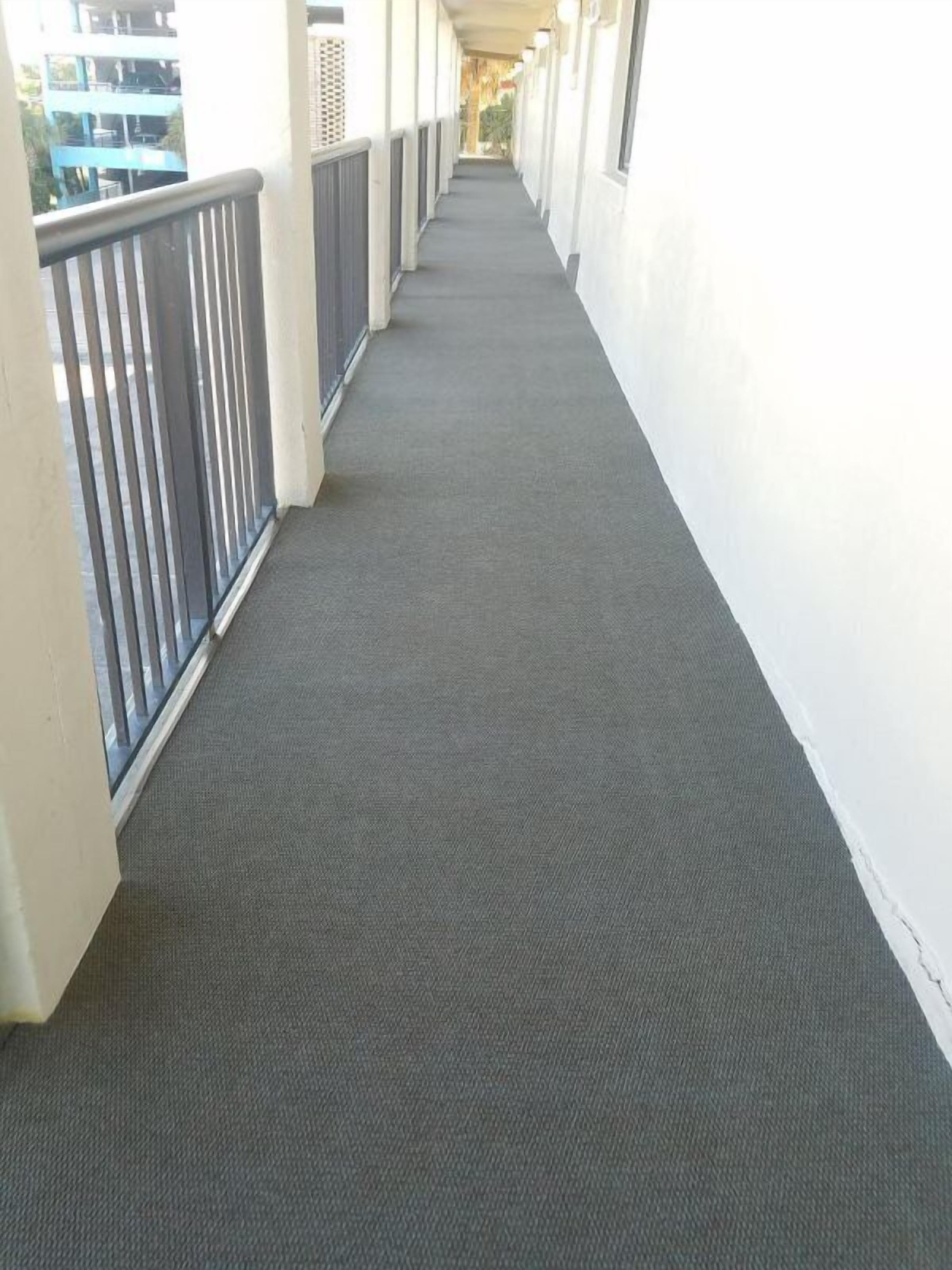 Un couloir avec un tapis gris, des murs blancs et une rambarde métallique d’un côté.