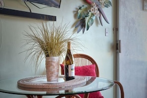 A small table with a potted plant and wine bottle sits in a room with a light-colored wall, accompanied by a chair with a cushion.