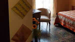 A room with a bed, a chair, a table with a vase of sunflowers, and decorative wall hangings. - Antico Palazzo (Piazza Armerina)