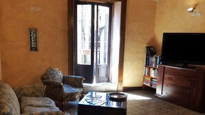 A living room with a sofa, armchair, coffee table, bookshelf, and a television. - Antico Palazzo (Piazza Armerina)