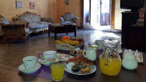 A living room with two sofas, a coffee table, and a television. There are various food items and drinks on the table. - Antico Palazzo (Piazza Armerina)