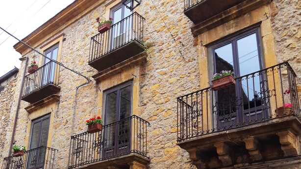 A stone building with multiple balconies, each with wrought iron railings and flower boxes. - Antico Palazzo (Piazza Armerina)