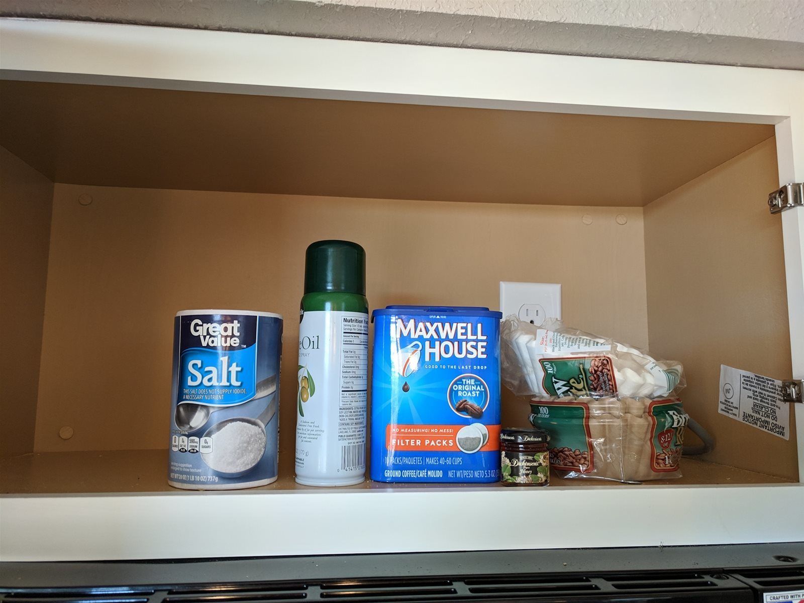 A shelf with Great Value Salt, a can of oil, Maxwell House Filter Packs, and some coffee beans.
