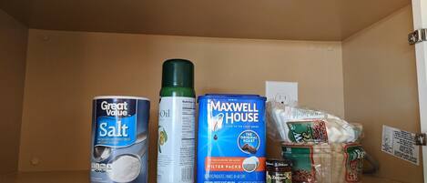 A shelf with Great Value Salt, a can of oil, Maxwell House Filter Packs, and some coffee beans.