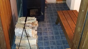 Un poêle à bois compact, doté d’une cheminée, avec une pile de bois de chauffage et un banc en bois.