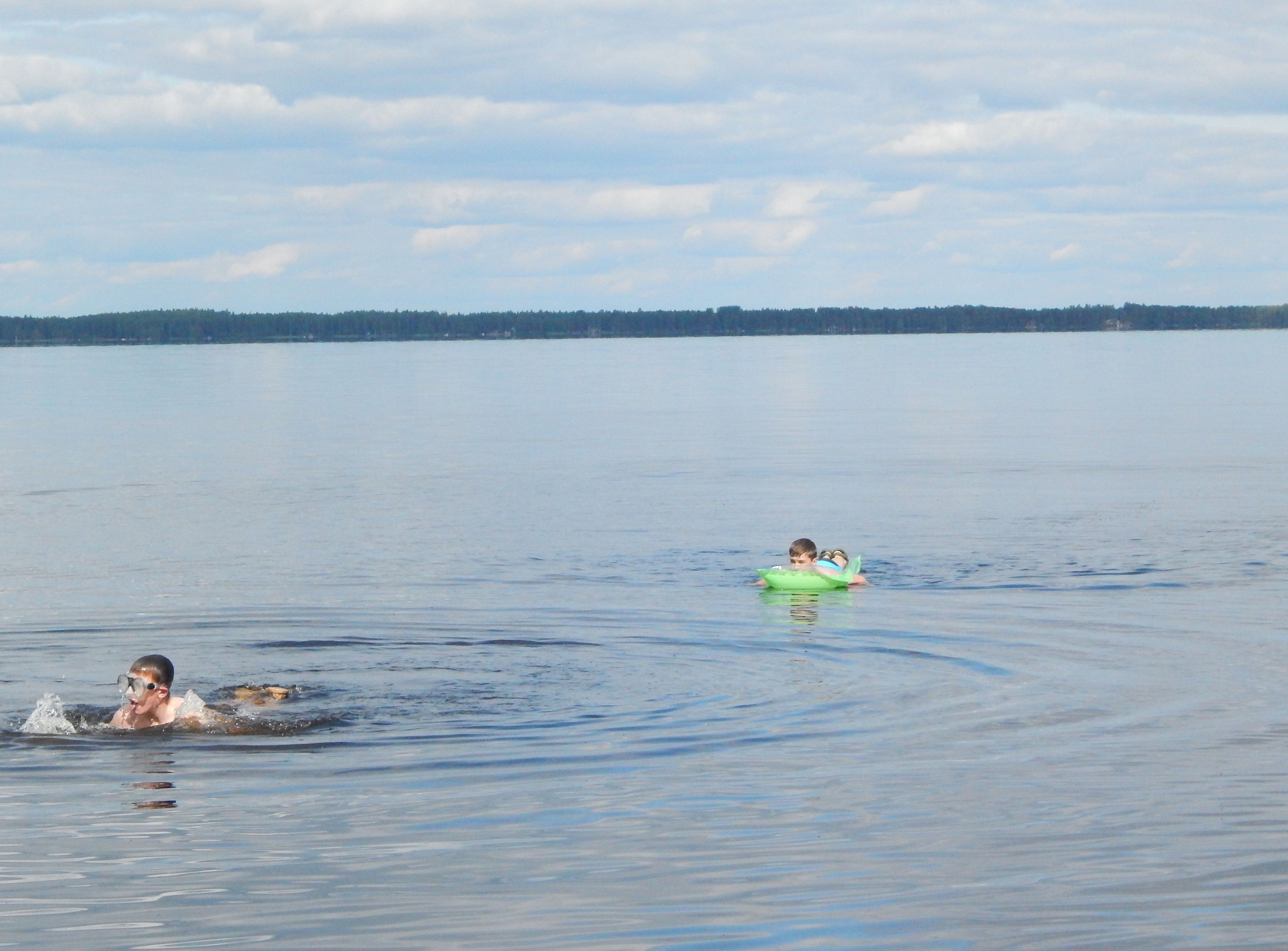 Un lago tranquilo con dos personas flotando en flotadores verdes.