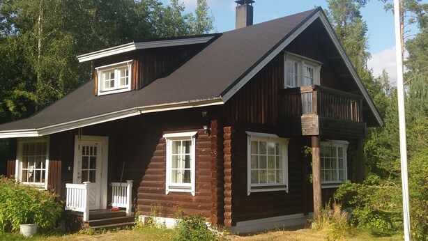 Une cabane en rondins avec un porche à l’avant, une cheminée et une pelouse bien entretenue agrémentée de fleurs.