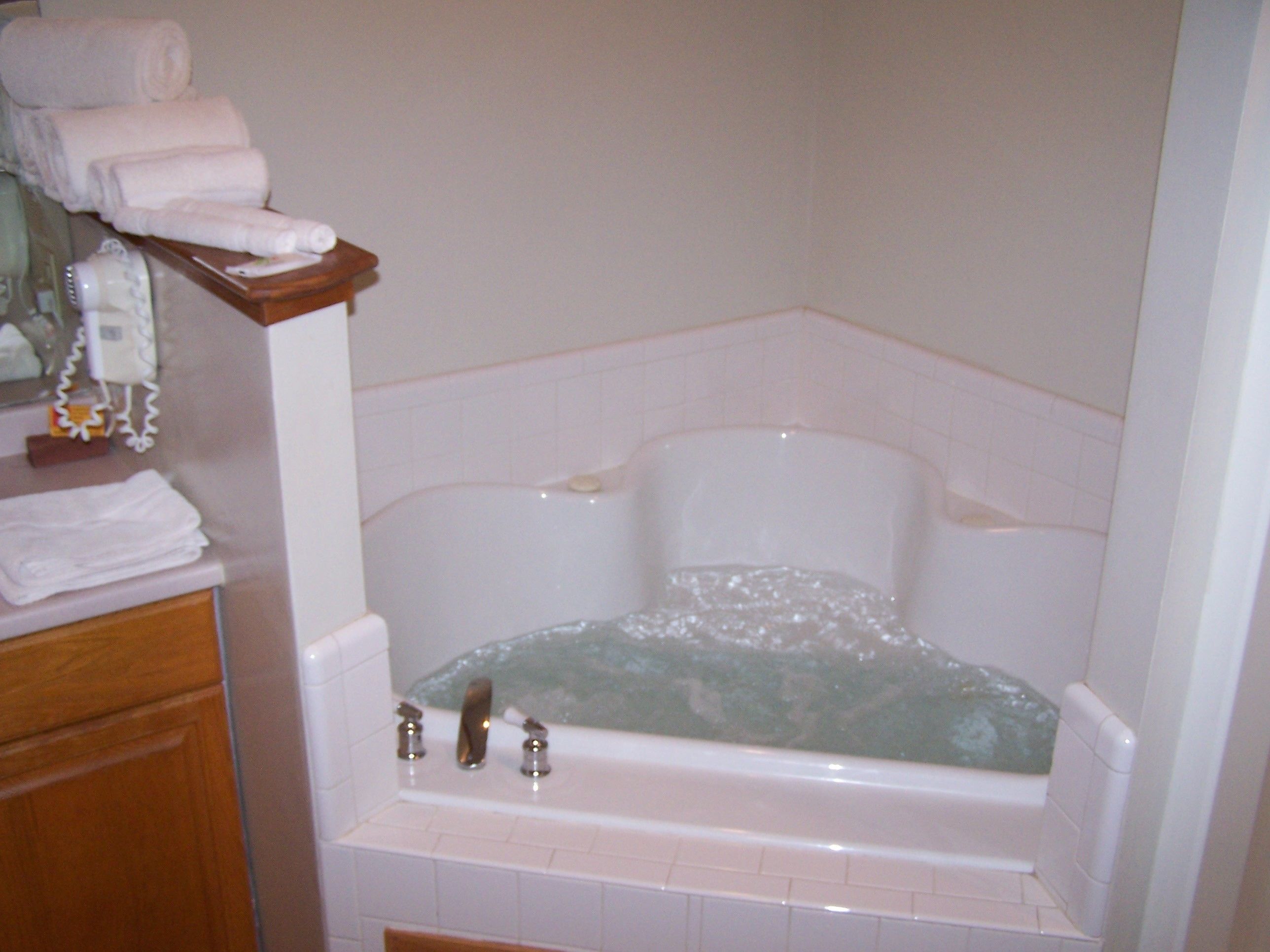 Une salle de bain avec une baignoire, une étagère en bois avec des serviettes et un miroir.