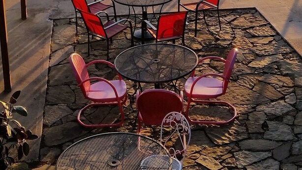 Espace extérieur aménagé avec des tables et des chaises, offrant une vue sur un plan d’eau et des collines.