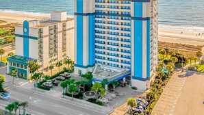 A hotel with a modern design, featuring a prominent blue and white color scheme, located near a beach with a clear view of the ocean. - Boardwalk 1030 (Myrtle Beach)