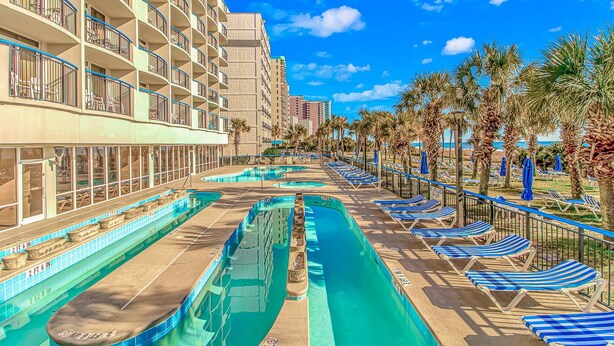 A hotel with multiple swimming pools, sun loungers, and palm trees. - Boardwalk 1030 (Myrtle Beach)