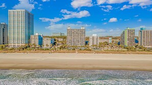 A beachfront hotel with multiple high-rise buildings, a sandy beach, and ocean waves. - Boardwalk 1030 (Myrtle Beach)