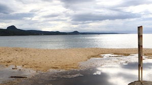 A beach with a metal post in the foreground, a calm sea, and mountains in the background. - Full Moon Resort (Hengchun)
