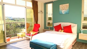A bedroom with a bed, two red pillows, a blue bench, a chair, and a view of greenery through a sliding door. - Full Moon Resort (Hengchun)