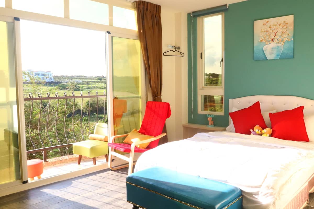 A bedroom with a bed, a chair, a small table, and a view of the outdoors.