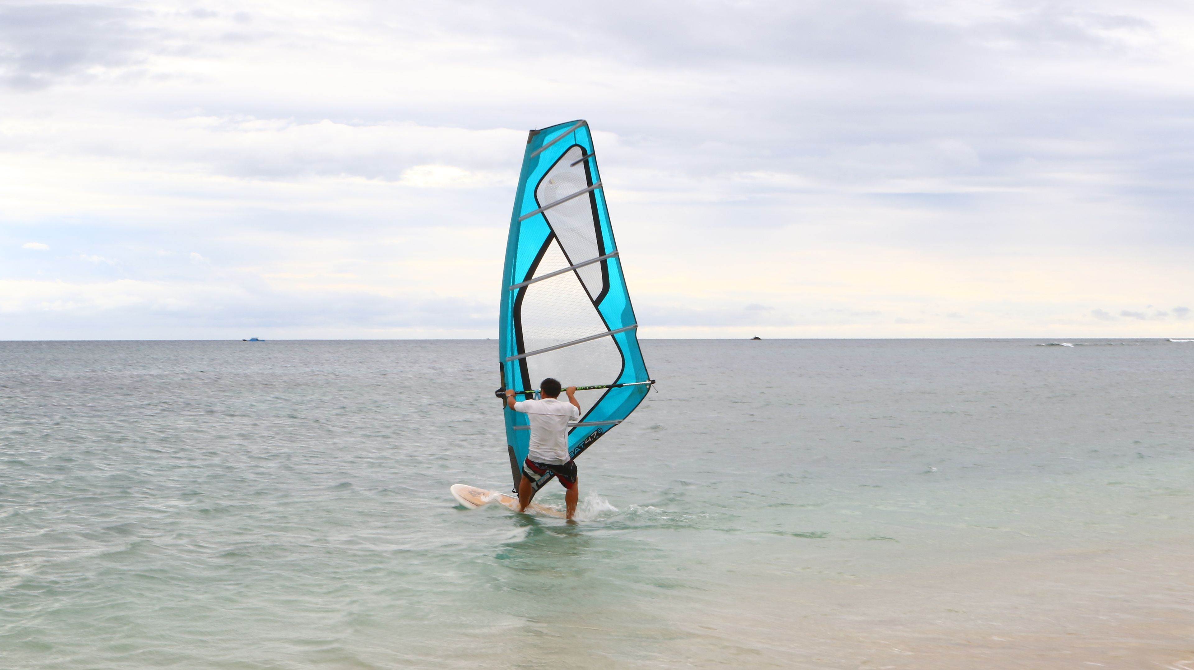 Una persona practica windsurf en un mar tranquilo bajo un cielo despejado.