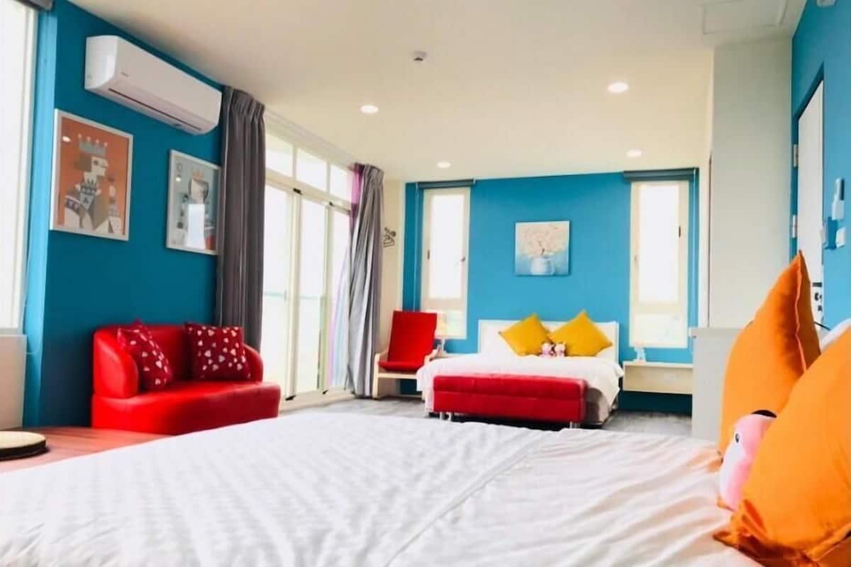A bedroom with a bed, a red sofa, a red armchair, and a window with curtains.