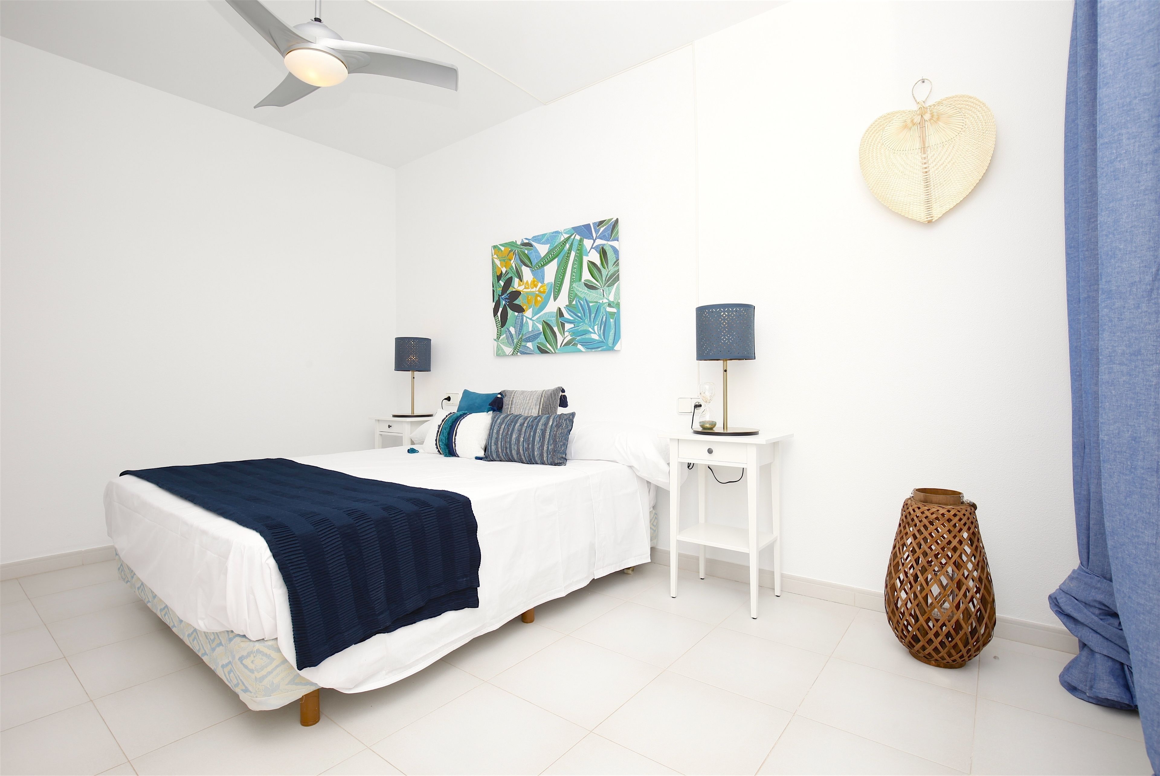 Een slaapkamer met een bed, nachtkastjes, een plafondventilator, een kunstwerk aan de muur en een decoratieve vaas.