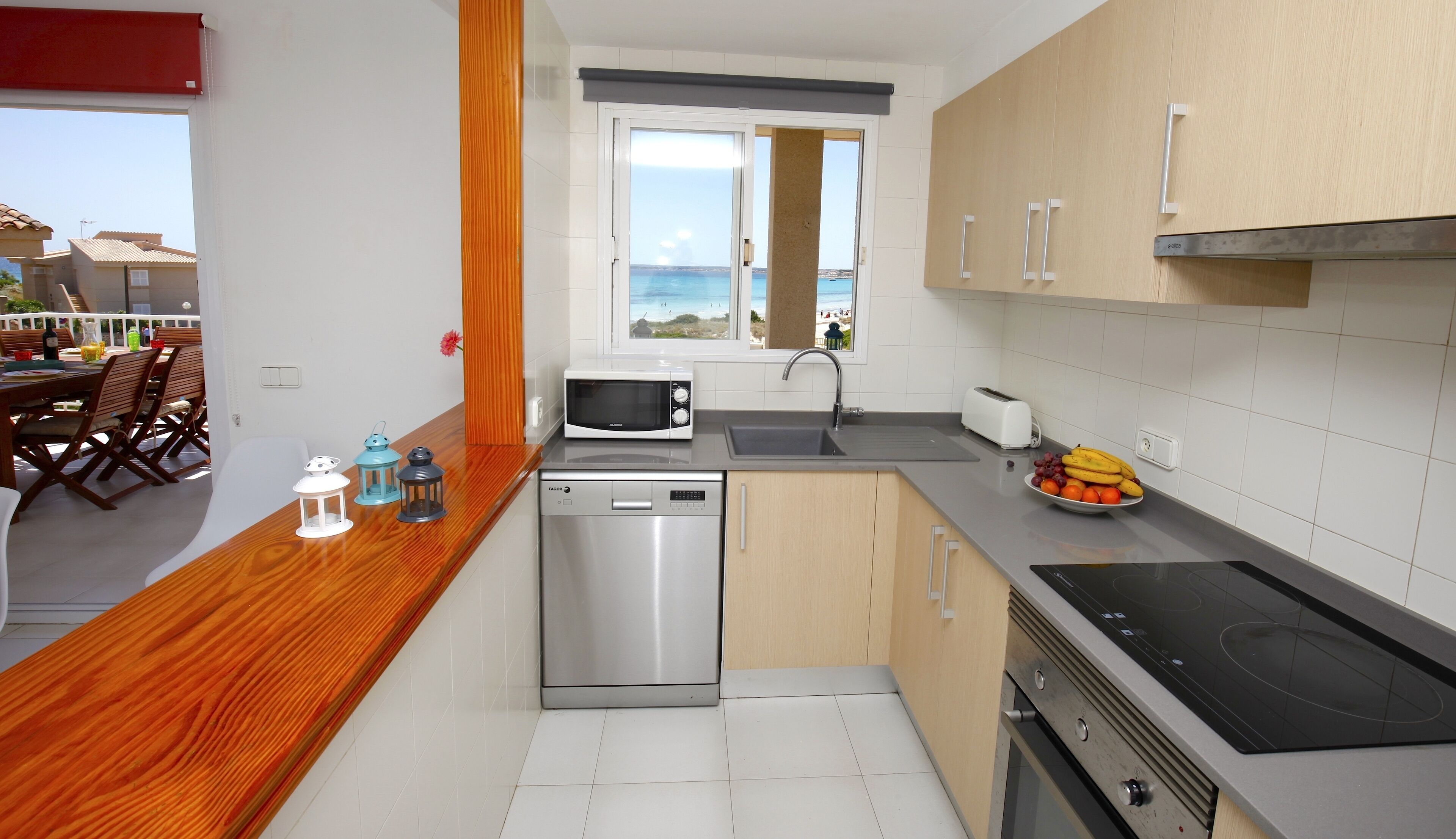 Cozinha compacta com máquina de lavar louça, micro-ondas e vista para o mar.