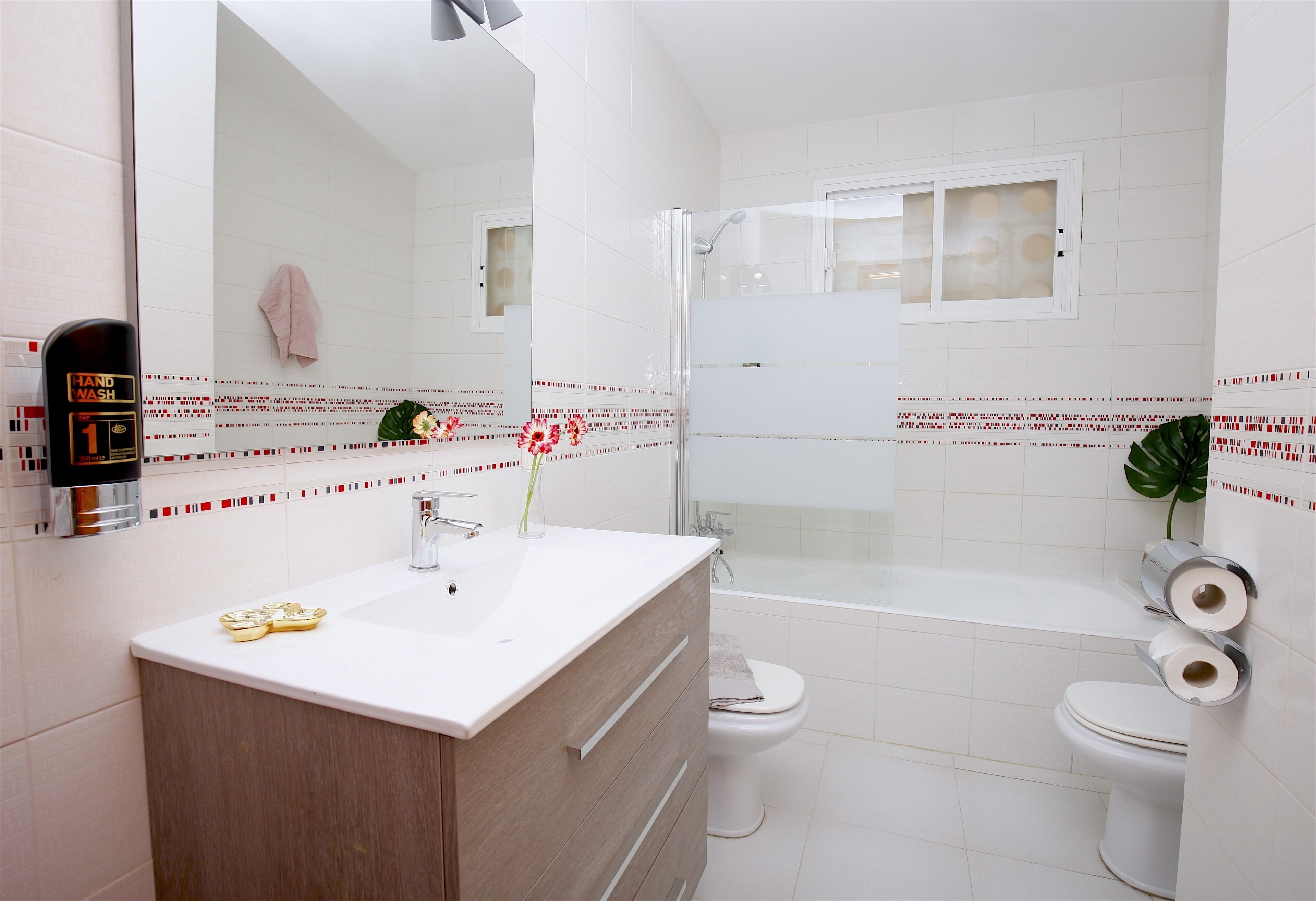 Une salle de bain moderne avec un lavabo blanc, deux toilettes, une douche et un miroir.