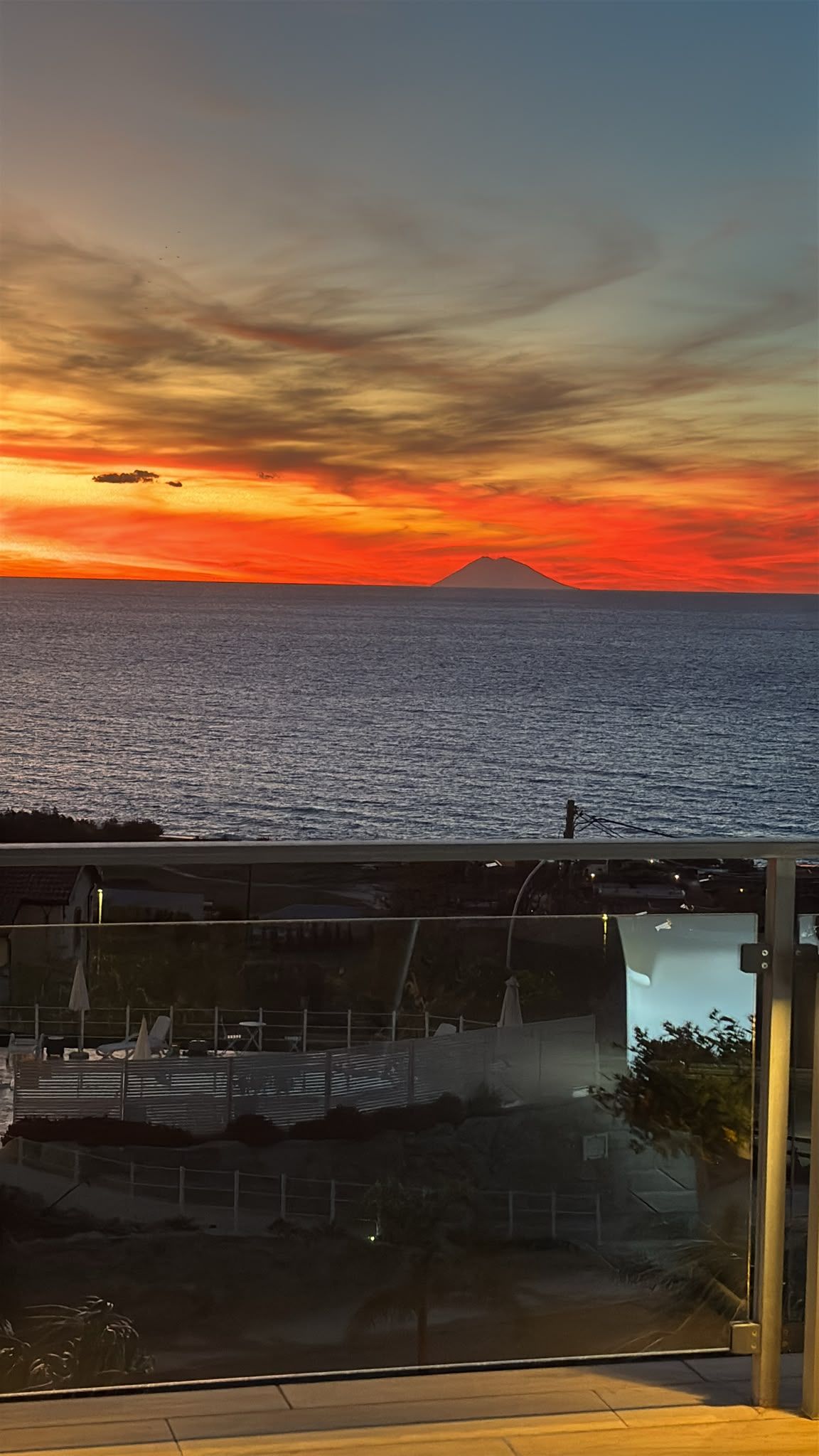 Sonnenuntergangblick von einem Balkon mit Pool und Liegestühlen.