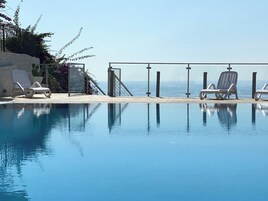 Una piscina cristalina con sillones de descanso y vista al mar.