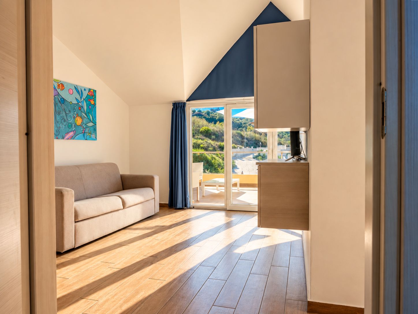 A modern living room with a sofa, a painting, and a view through a glass door to an outdoor area.