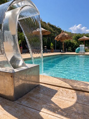 Una piscina con fuente de agua y un paraguas de paja.