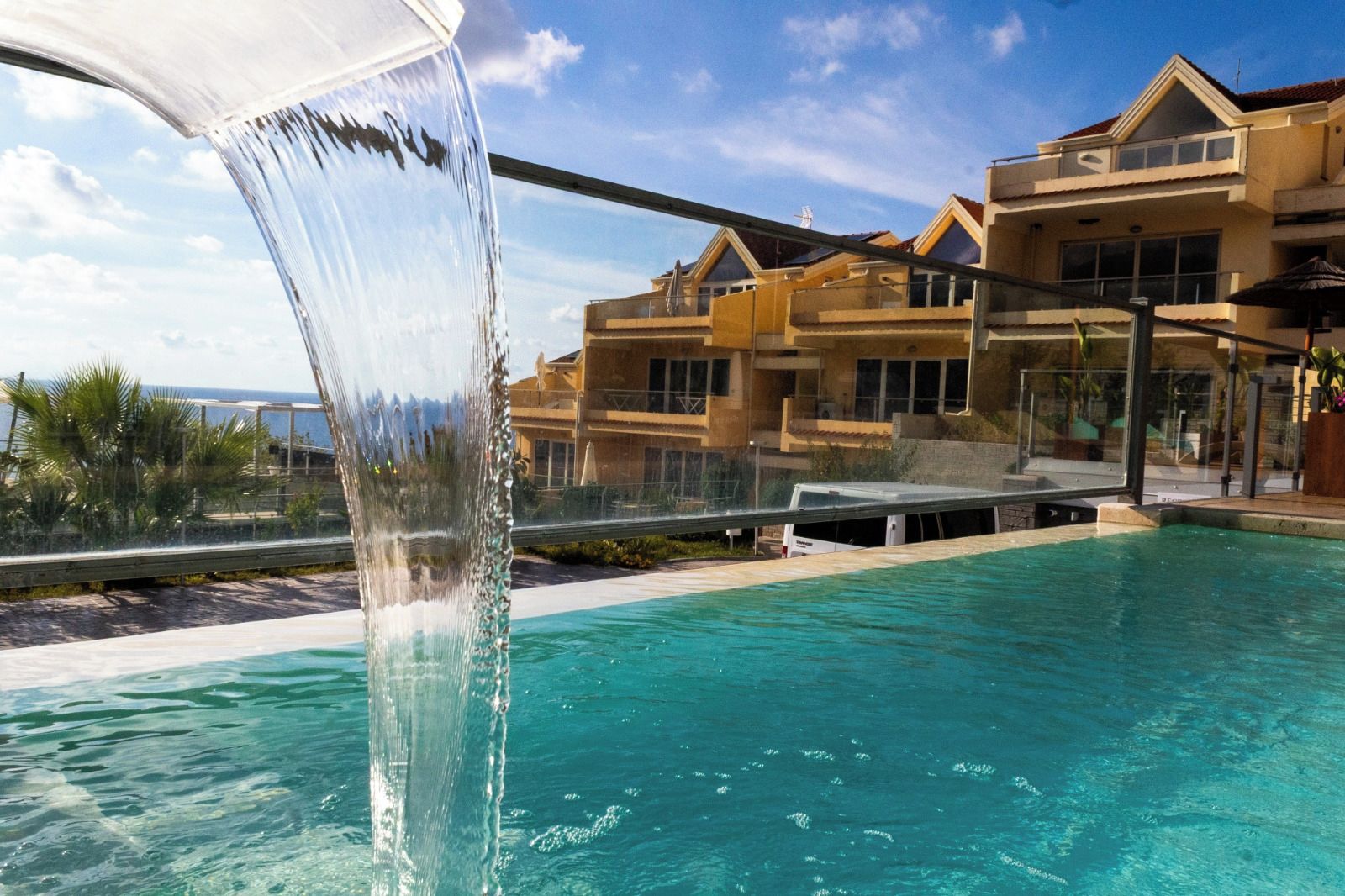 Una piscina con una cascata, circondata da edifici con balconi e ampie finestre.