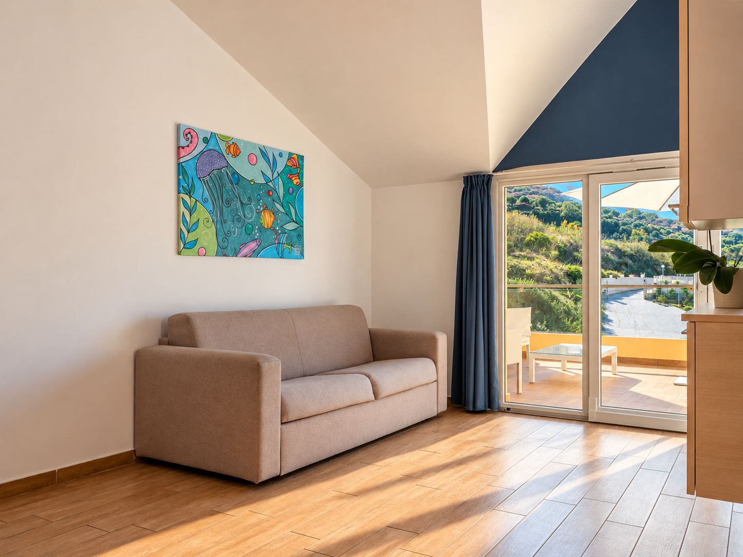 Ein modernes Wohnzimmer mit einer Couch, einem farbenfrohen abstrakten Gemälde und einer großen Glasschiebetür, die auf eine Terrasse mit Blick auf Grünflächen führt.